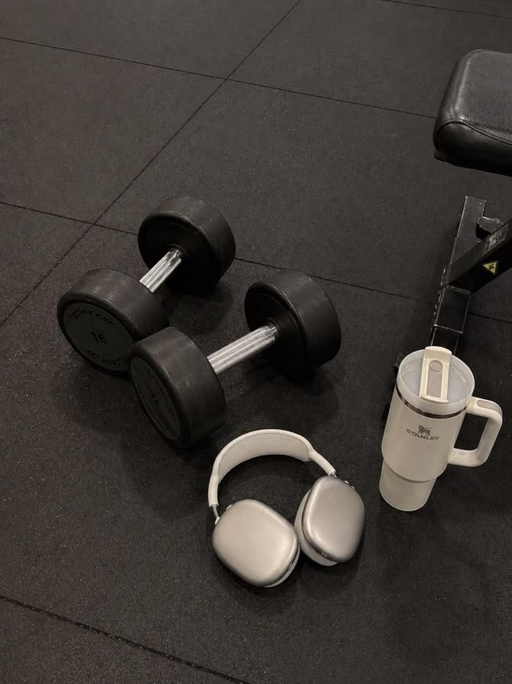 Mancuernas, auriculares y botella sobre el suelo del gimnasio antes de entrenar.