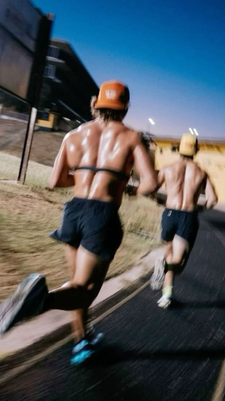 Dos corredores de espaldas subiendo una cuesta al anochecer.