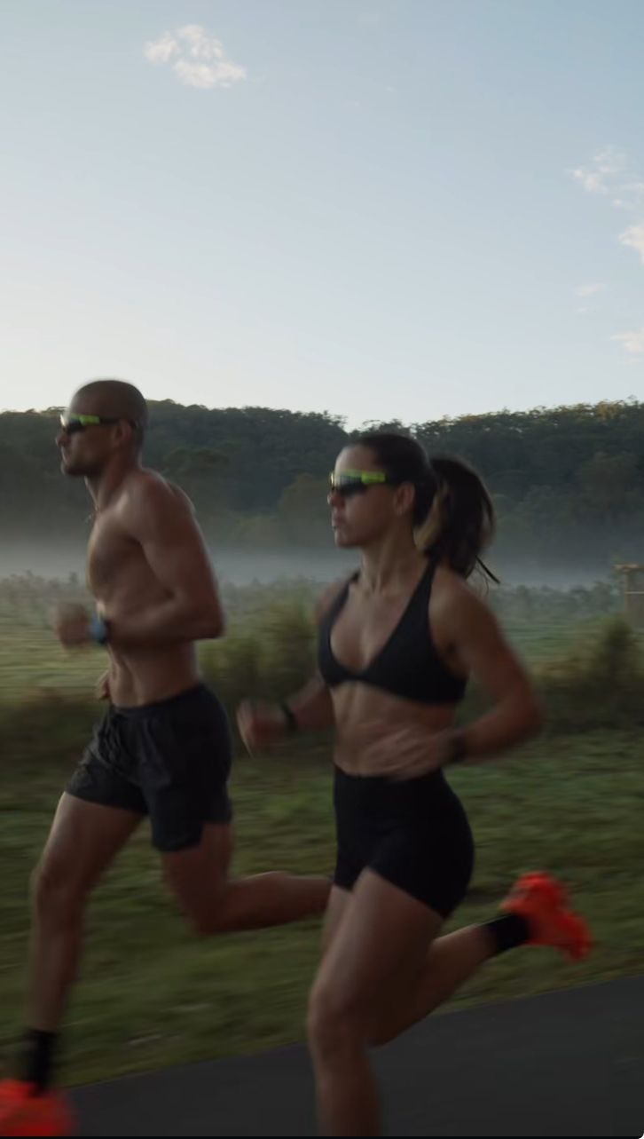 Dos personas corriendo juntas al amanecer por una carretera entre niebla.