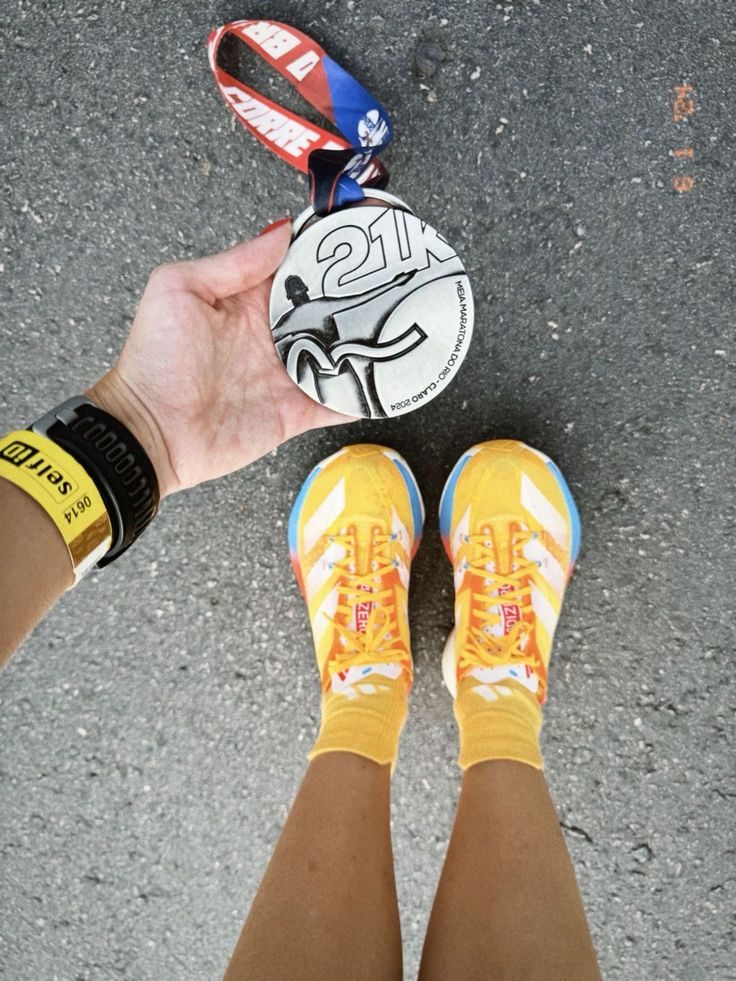 Corredora mostrando una medalla de 21K junto a sus zapatillas.